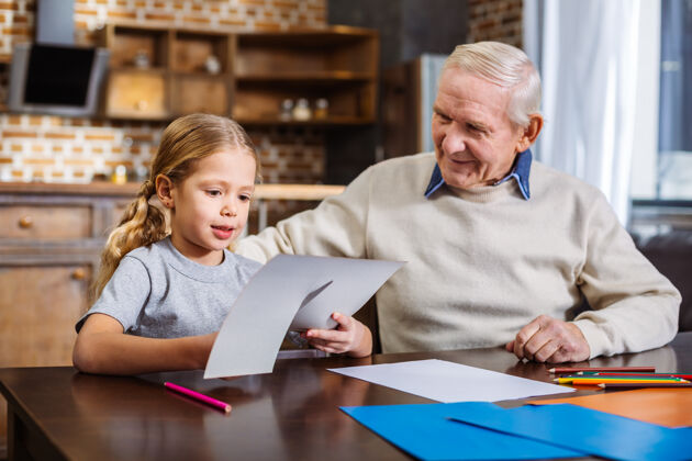 爱好可爱的小女孩和她的爷爷坐在桌边剪报纸幼儿园多彩厨房