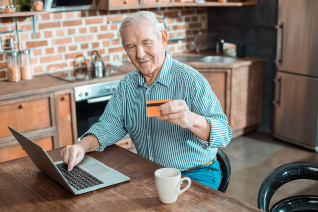 技术快乐善良的老人拿着一张信用卡 在使用笔记本电脑时在线支付老年人医疗保健养老金