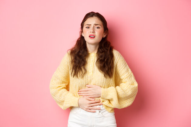 兴奋年轻女子肚子痛 手放在肚子上 感觉剧痛 月经来潮 站在粉红色的墙上时髦抽筋休闲