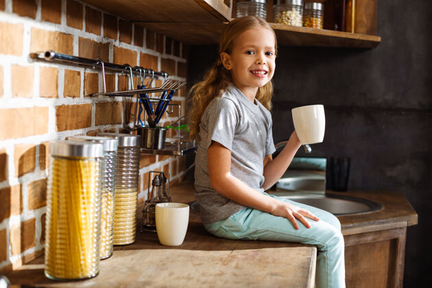新鲜可爱的小女孩在厨房喝茶时微笑着杯子牛奶快乐