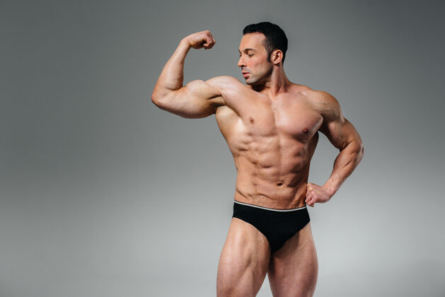 运动一个年轻的健美运动员赤裸上身在摄影棚里摆姿势 炫耀他的腹肌和肌肉运动运动员赤膊胸部