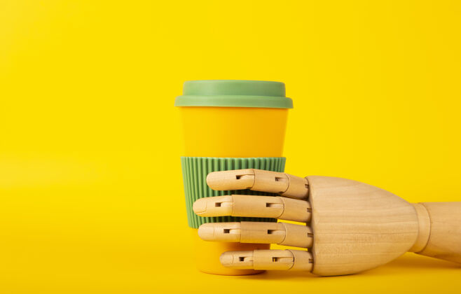 杯子木制人体模型手拿可重复使用的咖啡杯在一个黄色的表面微型人体模型回收