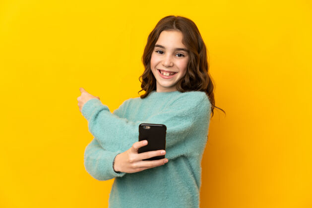 指着黄色背景下的白人小女孩用手机指着后面童年微笑智能