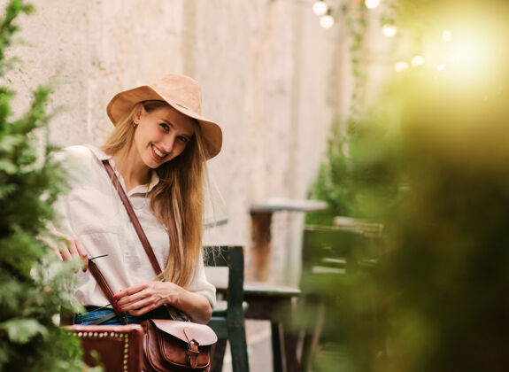 年轻年轻的金发女郎坐在复古风格的户外咖啡馆里看着相机咖啡馆街道时尚