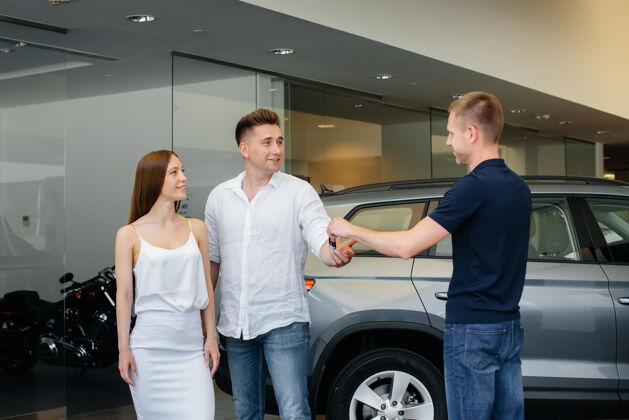 协议卖家把新车的钥匙递给一个年轻的家庭买一辆新车客户展厅年轻人