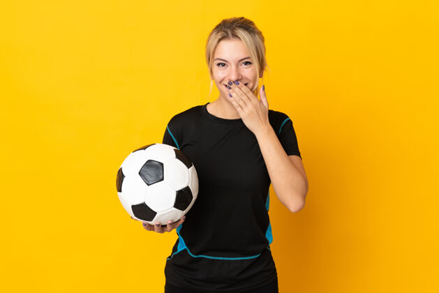微笑一个年轻的俄罗斯足球运动员 一个被隔离在黄色背景下的女人 幸福而微笑地用手捂住嘴球员成年人乐趣