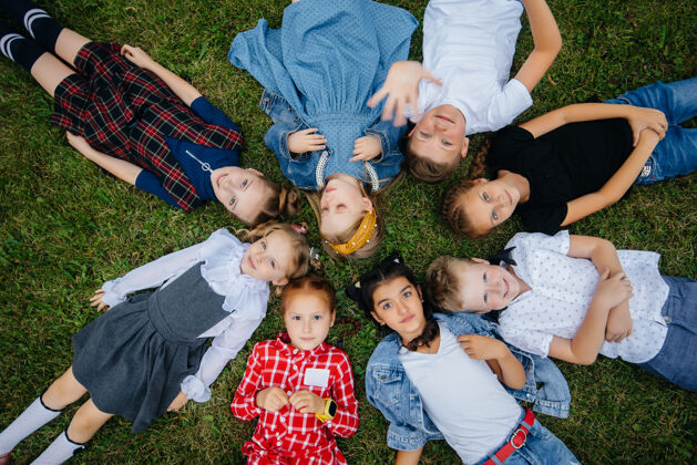 户外一群小学生围成一圈躺在草地上玩童年快乐花园友谊孩子