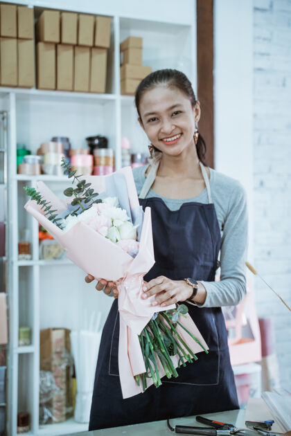 人在花店工作的快乐女花匠手持法兰绒花看着镜头女人商业商业
