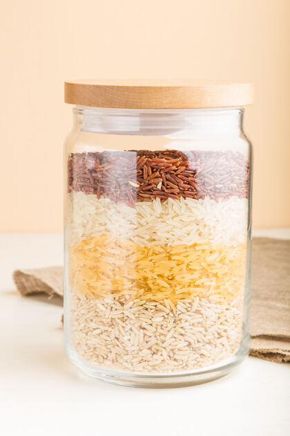 木材白色和橙色的表面上 一层一层地倒着各种大米的玻璃罐侧视图 特写素食者储藏食物
