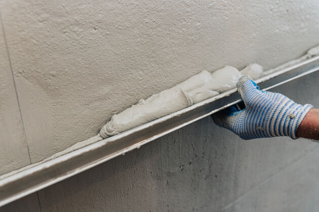 翻新粉刷墙壁的最后阶段一个工人用水平仪把灰泥找平手工水泥房屋