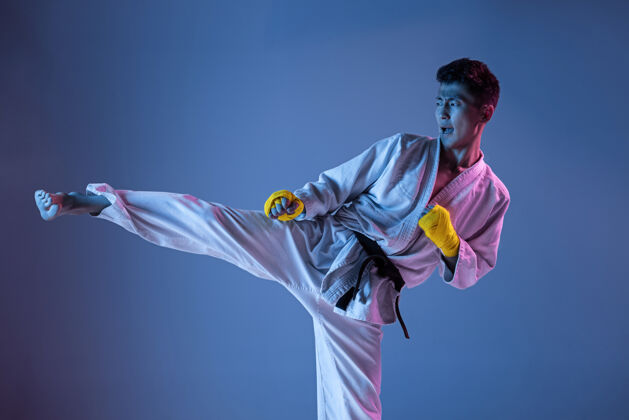 拳打自信的韩国人穿着和服练习徒手格斗 武术年轻的男子拳击手在霓虹灯下用黑带在梯度背景上训练健康的生活方式 运动的概念动作攻击动作