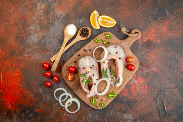 切割新鲜生鱼和胡椒洋葱绿色西红柿的俯视图在混合色表面上的木制砧板上烹饪容器食物