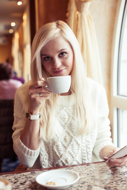 咖啡馆女人的手拿着一杯热可可一个年轻的女人坐在一个舒适的房间里咖啡馆女孩在喝酒可可冬天舒适秋天热的室内风景