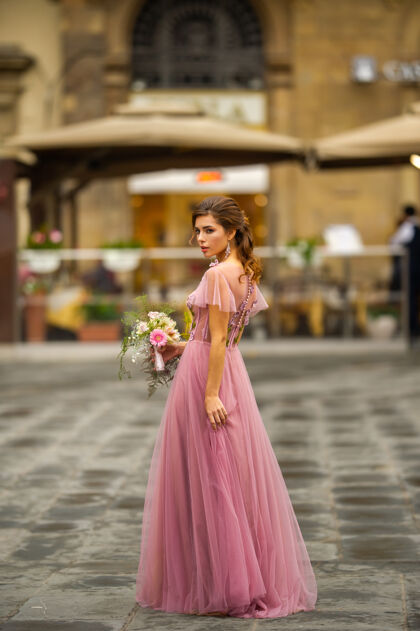 婚纱意大利佛罗伦萨古城中心站着一位身穿粉色礼服 手持花束的新娘礼服女孩魅力