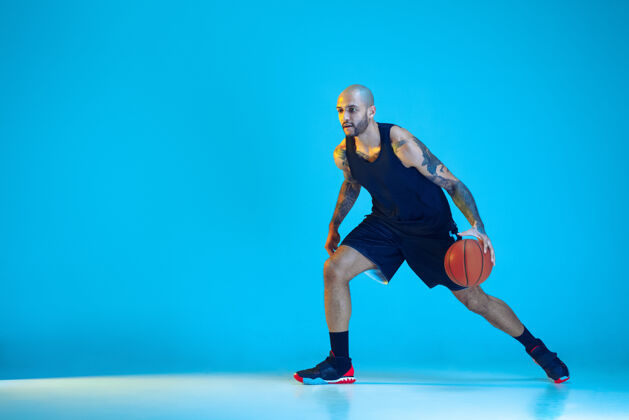 活跃年轻的篮球队员穿着运动服训练 在运动中练习 在霓虹灯下的蓝色背景下孤立运动运动的概念 运动 活力和活力 健康的生活方式年轻强壮肌肉