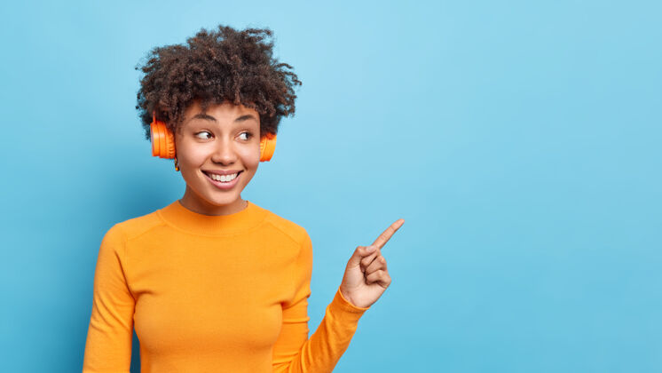 女性横向拍摄的美籍黑人女性听音轨穿着休闲橙色套头衫点在蓝色复制空间建议检查促销演示公告促销指向乐观