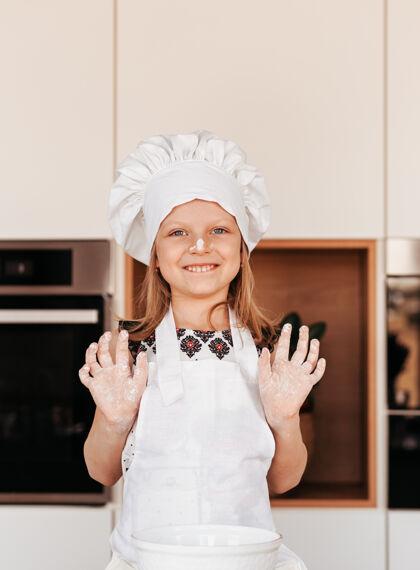 围裙一个戴着白色厨师帽的有趣小女孩在厨房里玩面粉厨房宝贝厨师手年轻肖像