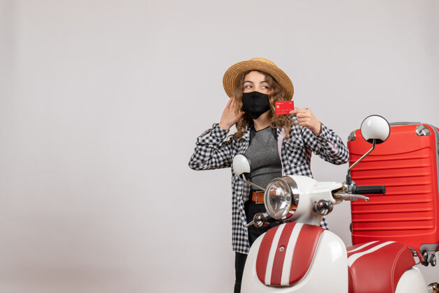 手提箱正面图：戴着黑色面具的年轻女子手持卡片站在红色轻便摩托车旁边面罩冒险度假