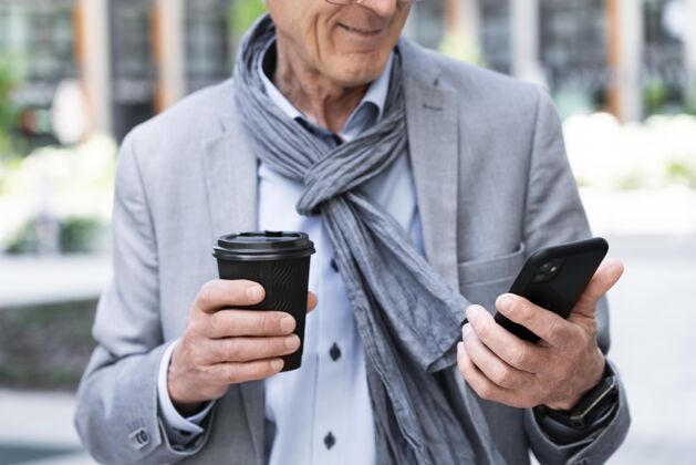 城市城里时髦的老人一边喝咖啡一边用智能手机老年人老年人户外