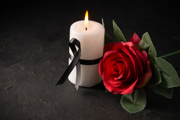 打蜡黑上有红玫瑰的白蜡烛的正视图红玫瑰烛光