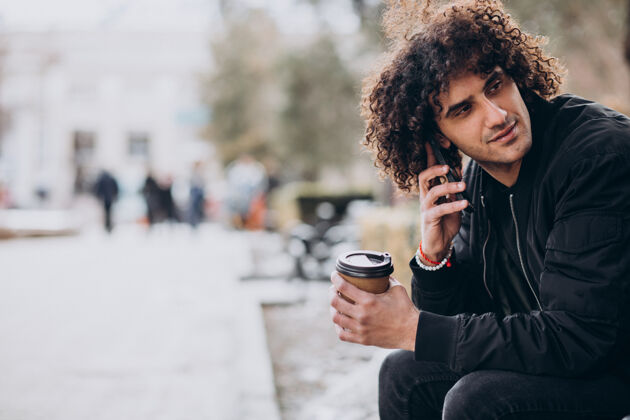 时髦卷发的年轻人一边喝咖啡一边打电话外卖黑发城市