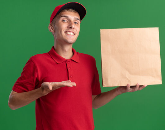 持有微笑着的年轻金发送货员抱着并指着纸包裹年轻包装点