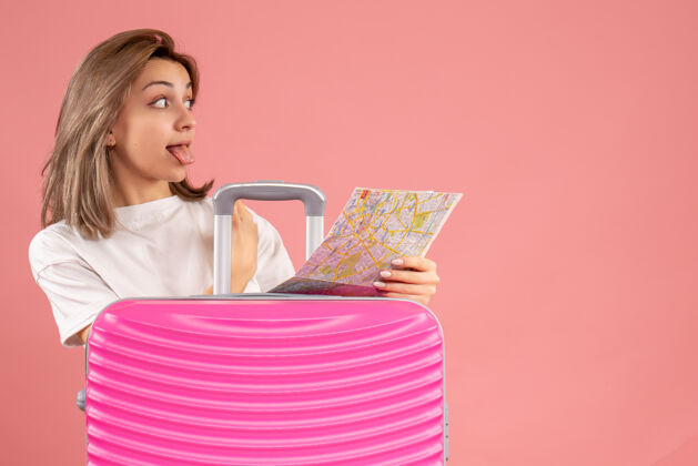 冒险正面图：一位年轻女士 手拿粉色手提箱 伸出舌头 拿着地图肖像旅游成人