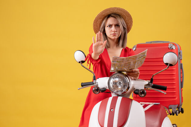 人正面图身穿红色连衣裙的年轻女士手持地图 在轻便摩托车旁做停车标志旅游肖像手提箱