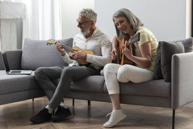 室内资深夫妇在家学习吉他和四弦琴课程的笔记本电脑沙发水平灰色头发