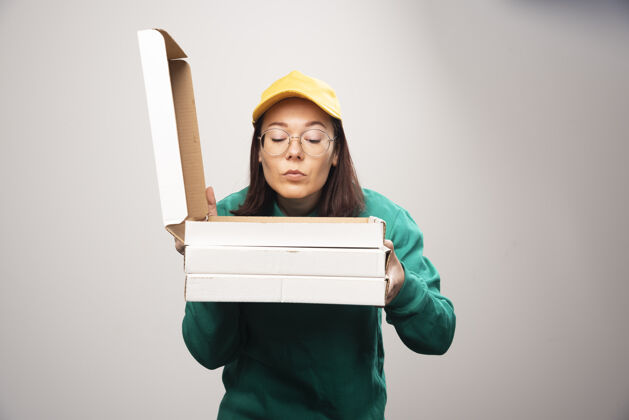 芳香女送货员在一张白色的高质量的照片上看披萨的纸板快递制服姿势
