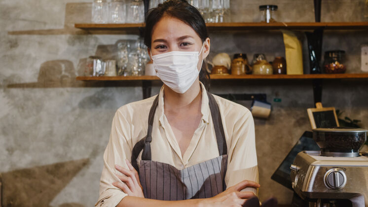 重新开放肖像年轻的亚洲女孩女服务员戴着医用面罩 在市区咖啡馆被锁后 心情愉快地微笑着等待客人拉丁语年轻人看相机