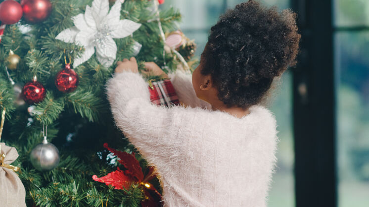 玩具圣诞树上装饰着装饰品的非洲裔美国小孩新的庆祝女人