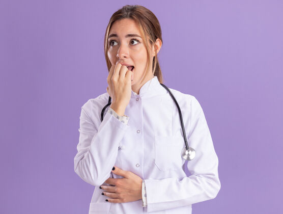 穿关心的看着身边年轻女医生穿着医用长袍用听诊器咬指甲隔离在紫色的墙上人医生表情