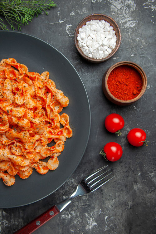 盘子在一个黑色的盘子里 用叉子叉上不同的调味品 在一张深色的桌子上放上西红柿 吃半杯简单的意大利面午餐胡椒番茄