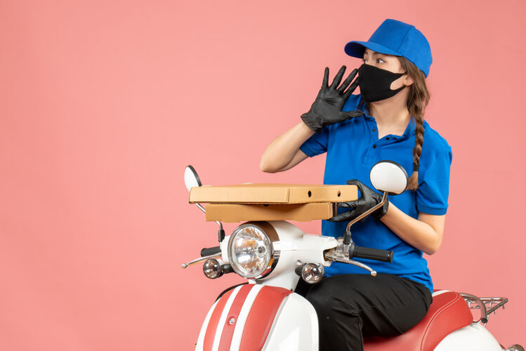 面具俯视图：年轻的女快递员戴着医用口罩和手套坐在滑板车上 用粉彩桃子传递订单手套视图顶部