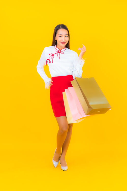 购物者一位年轻漂亮的亚洲女士 手拿购物袋 信用卡 黄色肖像销售欢呼