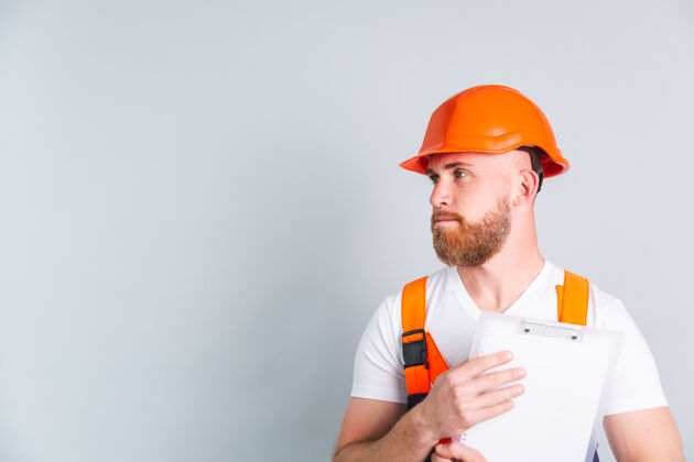 展示帅哥工程师在灰色墙上盖防护帽拿着白色剪贴板成人职业业务