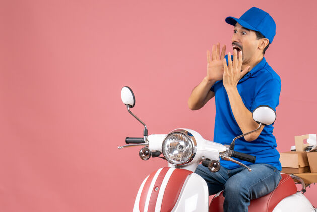 人俯视图：戴着帽子的快递员坐在滑板车上 在柔和的桃色背景下传递订单摩托车摩托车背景