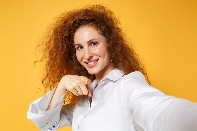 女性特写镜头：穿着白衬衫的年轻红发女子在黄橙色的墙上孤零零地摆姿势人物特写红发