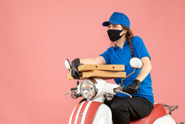 医学顶视图年轻好奇情绪化的女快递员戴着医用面罩和手套坐在滑板车上传递粉彩桃的订单桃坐滑板车