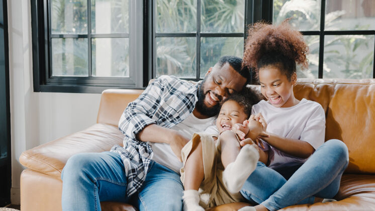 女人快乐快乐的非洲裔美国人家庭爸爸和女儿在家过生日时在沙发上玩得很开心笑女儿放松