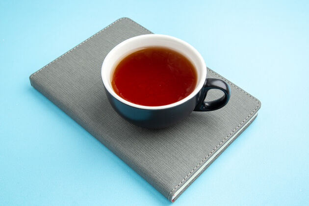 杯子蓝色表面上的灰色笔记本上的一杯红茶的正视图茶茶碟早餐