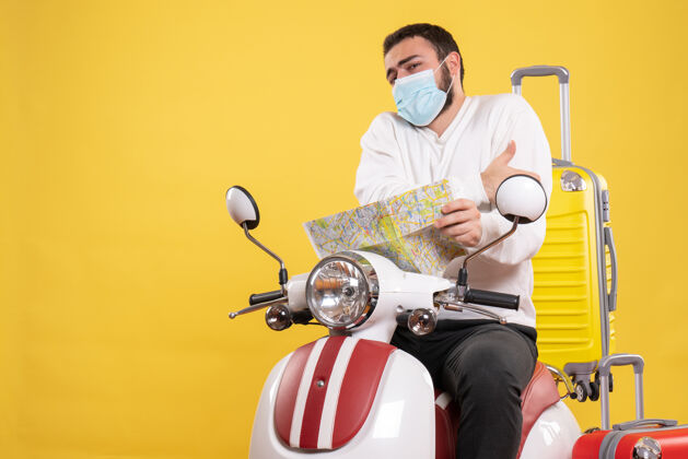 肩膀旅行概念 戴着医用面罩的年轻人坐在摩托车上 黄色手提箱在上面男人摩托车坐着