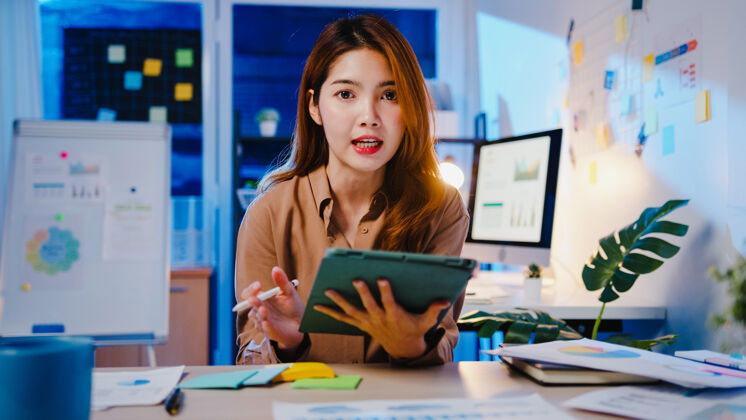 自由职业者亚洲女商人社交距离在病毒预防的新常态中看着摄像机向同事演示在办公室晚上工作时的视频通话计划个人住宅通信