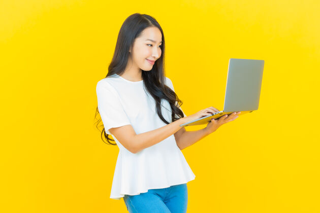 女性一幅美丽的亚洲年轻女子微笑的画像 黄色的笔记本电脑惊奇办公室中文
