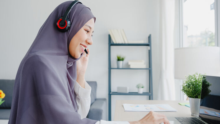远程亚洲女士戴着耳机看网络研讨会听在线课程在家里通过电话会议视频沟通呼叫战略商务妇女