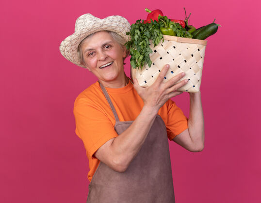 蔬菜微笑的上了年纪的女园丁戴着园艺帽 肩上扛着菜篮子微笑粉色老人