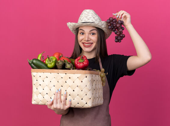 花园漂亮的白人女园丁戴着园艺帽 手里拿着菜篮子和一串葡萄漂亮蔬菜女