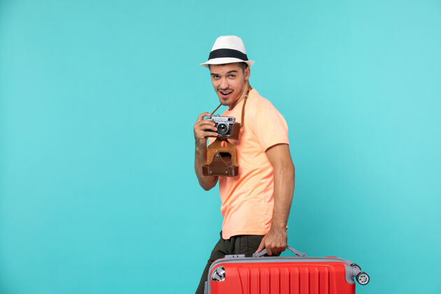包带着他的大红色手提箱和相机在蓝色的天空上拍照的度假男人男人旅行大