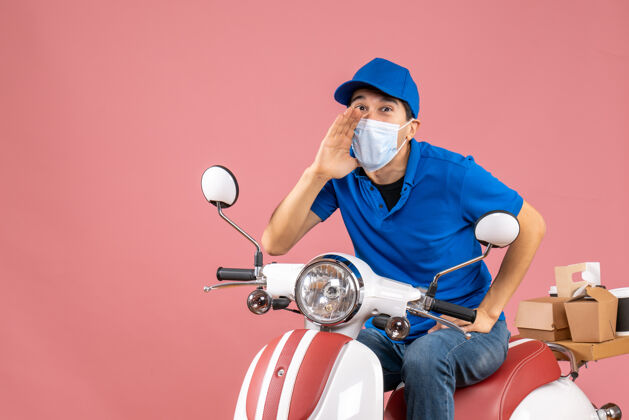 摩托车俯视图微笑的快递员戴着医用面罩戴着帽子坐在滑板车上 用柔和的桃色呼唤着某人医疗摩托车桃